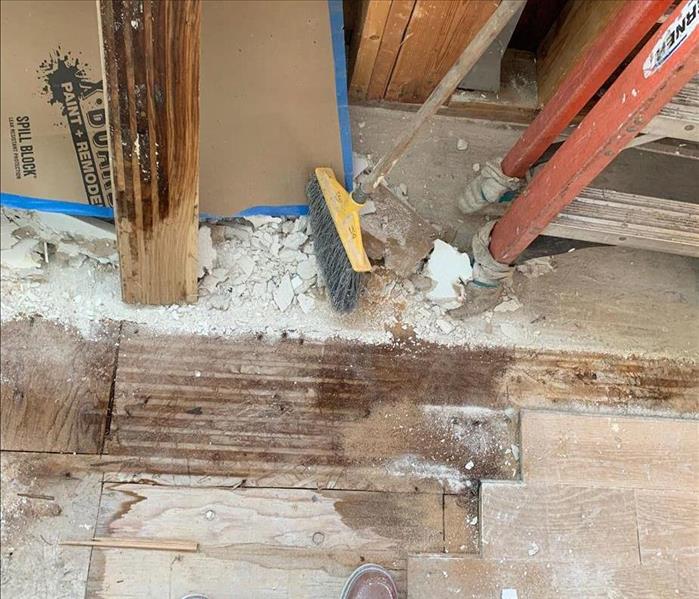 Visible debris on floor near wet wall framing, subfloor, and partially-removed flooring