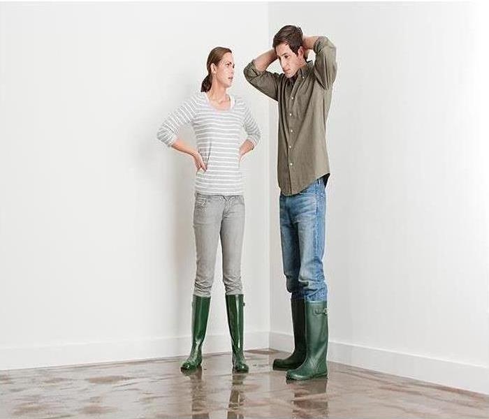 Two people in rubber boots standing in a flooded home